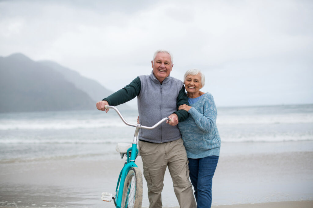 senior couple standing with bicycle beach